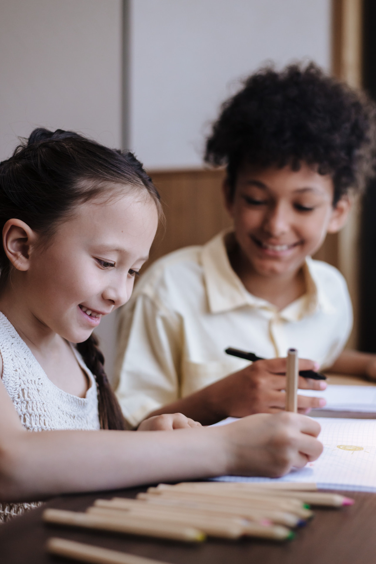 Two students smiling while writing in notebooks during a tutoring session